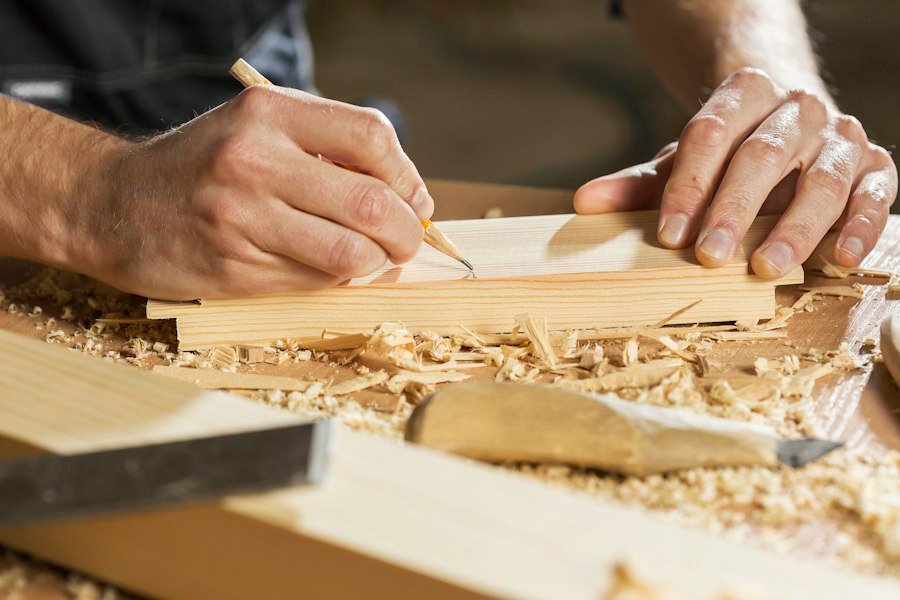 Hands marking a cut line on a wooden board with a pencil